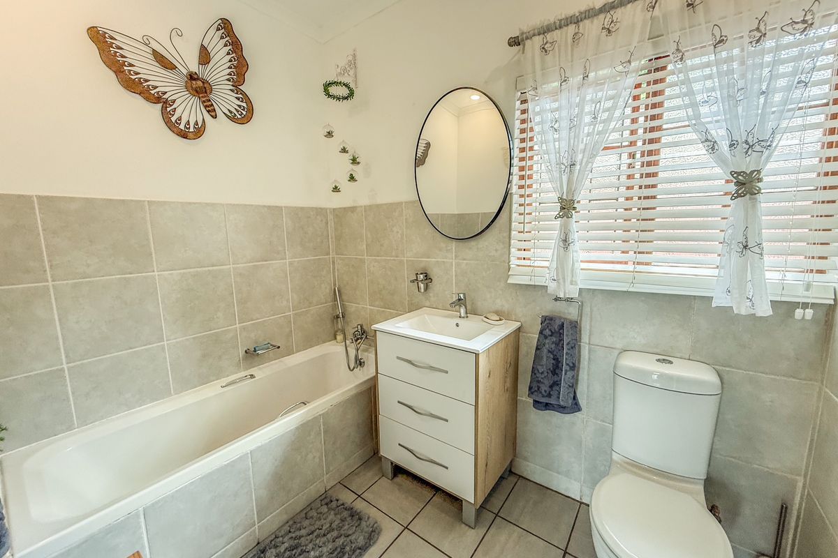A well-maintained bathroom featuring a built-in bathtub, a modern vanity with integrated sink, and a standard toilet with neutral wall and floor tiling.
