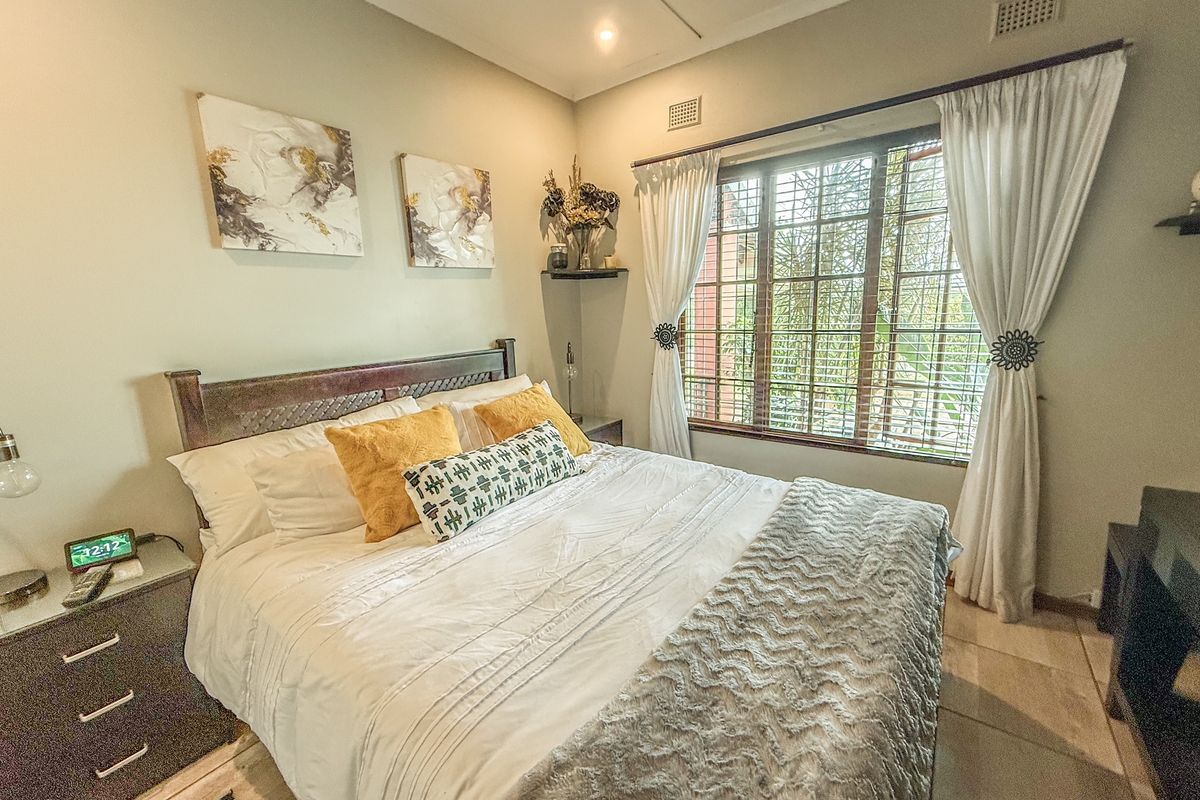 A well-lit bedroom featuring tiled flooring, a large window with security bars, and integrated ceiling ventilation.