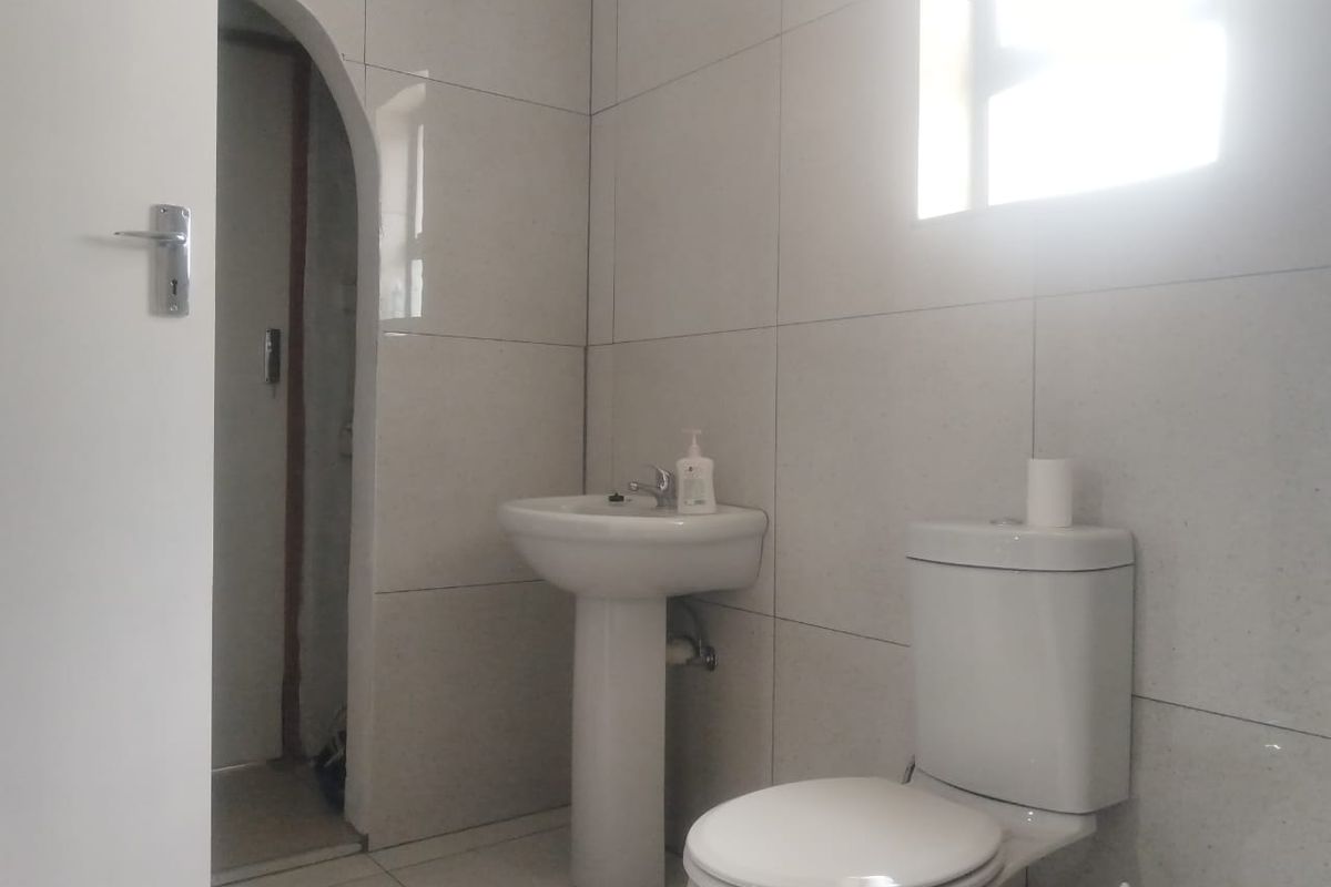A functional bathroom featuring floor-to-ceiling wall tiles, a pedestal basin, and a standard toilet, with an arched doorway leading to an adjacent space.