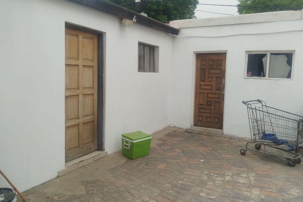 A rear exterior courtyard area featuring paved flooring and access to two separate entry points with wooden doors.