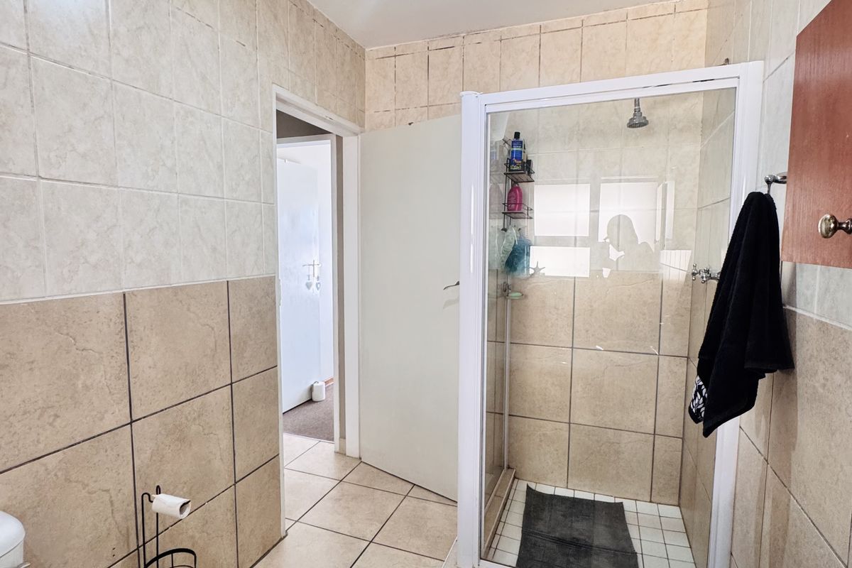 A functional bathroom featuring a glass-enclosed shower, tiled walls and flooring, and standard sanitary fixtures.