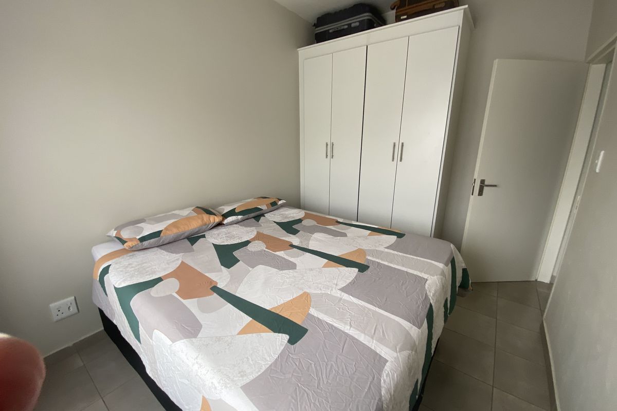 A functional bedroom featuring built-in white cabinetry and neutral floor tiling, providing a clean and practical living space.