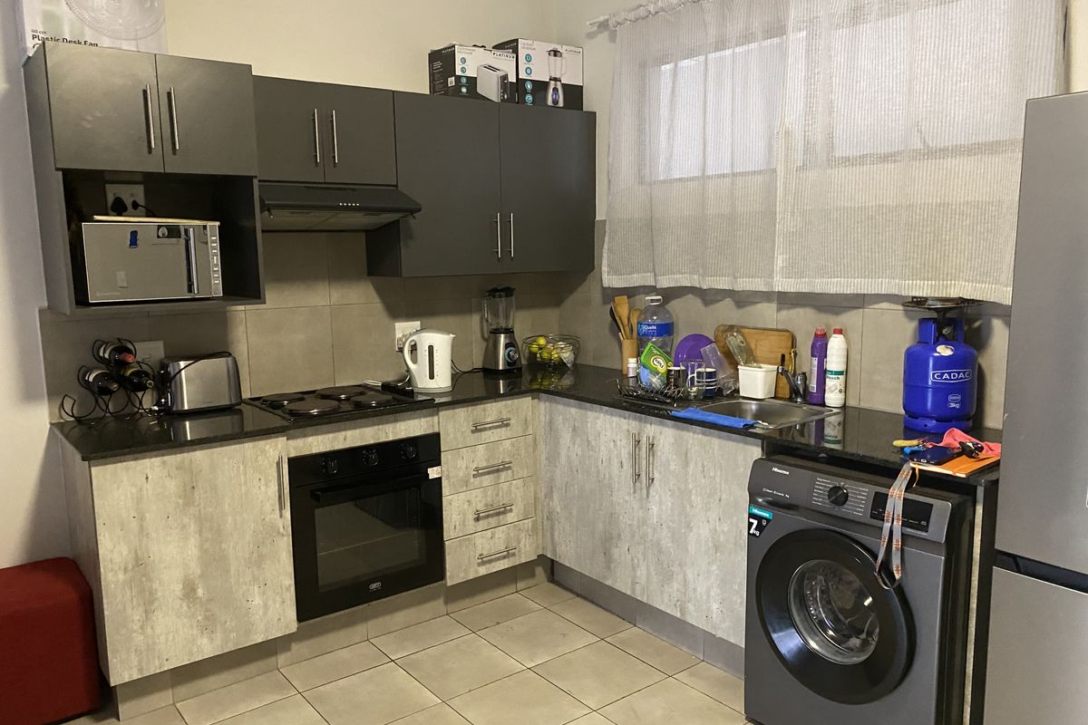 A functional kitchen featuring dark upper cabinetry, light-toned lower cabinets, a built-in oven, hob, extractor fan, and integrated space for a washing machine.