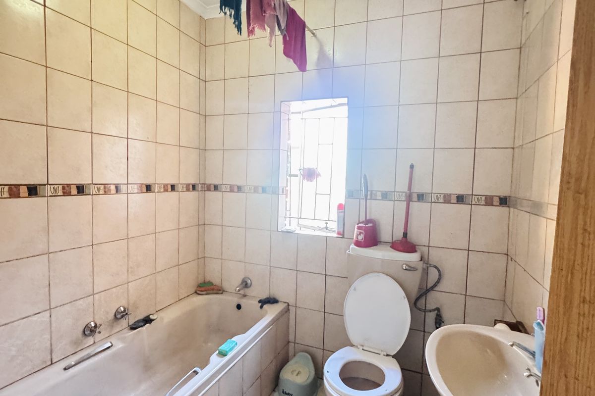 A compact bathroom featuring a built-in bathtub, a standard toilet, and a wall-mounted basin with tiled walls and flooring.