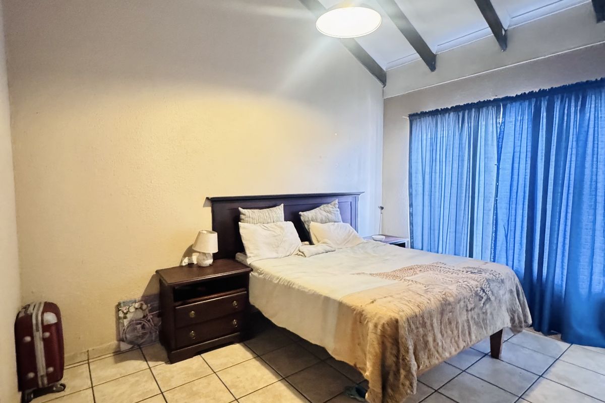 Spacious bedroom featuring high vaulted ceilings with exposed timber beams and large windows with blue curtains, finished with neutral ceramic floor tiles.