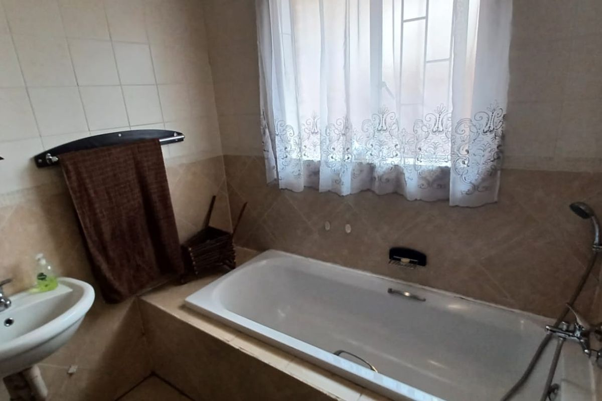 A functional bathroom featuring a built-in bathtub with a handheld shower attachment, a wall-mounted basin, and tiled wall finishes.