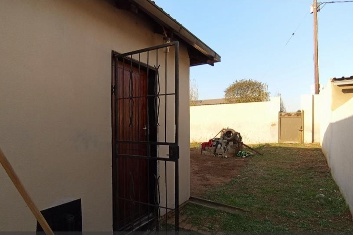 A view of the rear exterior area featuring a security gate, perimeter boundary walls, and an open yard space.