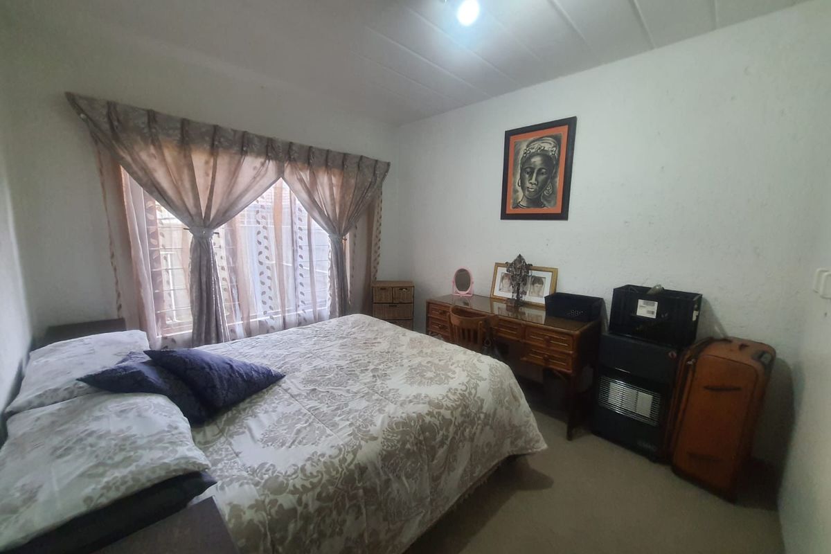 A functional bedroom featuring carpeted flooring and a large window with curtain treatments, providing a comfortable and private sleeping space.