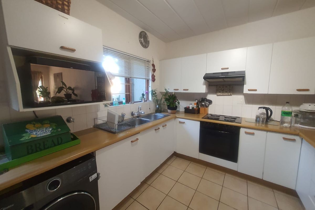 Functional kitchen featuring white cabinetry, laminate countertops, integrated oven, hob, extractor fan, and double basin sink with tiled splashbacks.