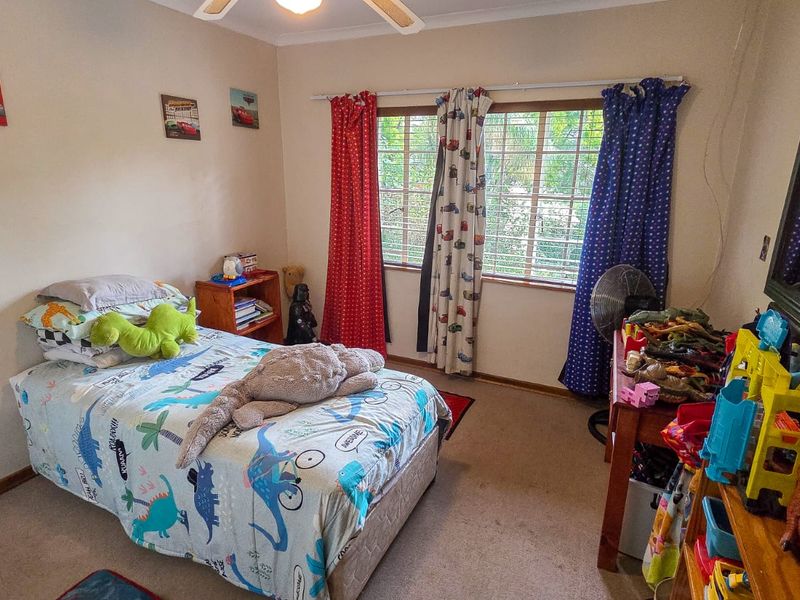 A standard bedroom featuring a ceiling fan and window security bars, providing a functional space with neutral wall finishes.