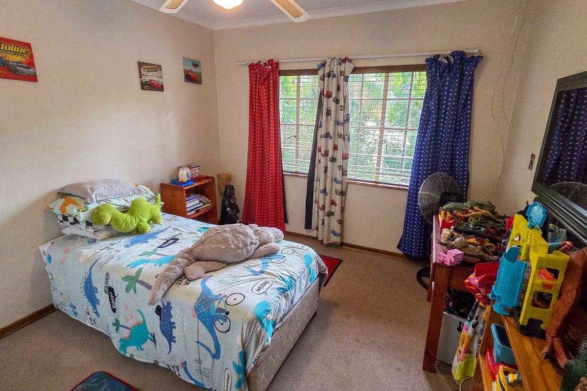 A standard bedroom featuring a ceiling fan and window security bars, providing a functional space with neutral wall finishes.