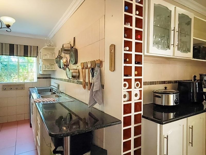 A functional kitchen featuring granite countertops, ample built-in cabinetry, a dedicated wine rack, and a double basin sink with tiled backsplash.