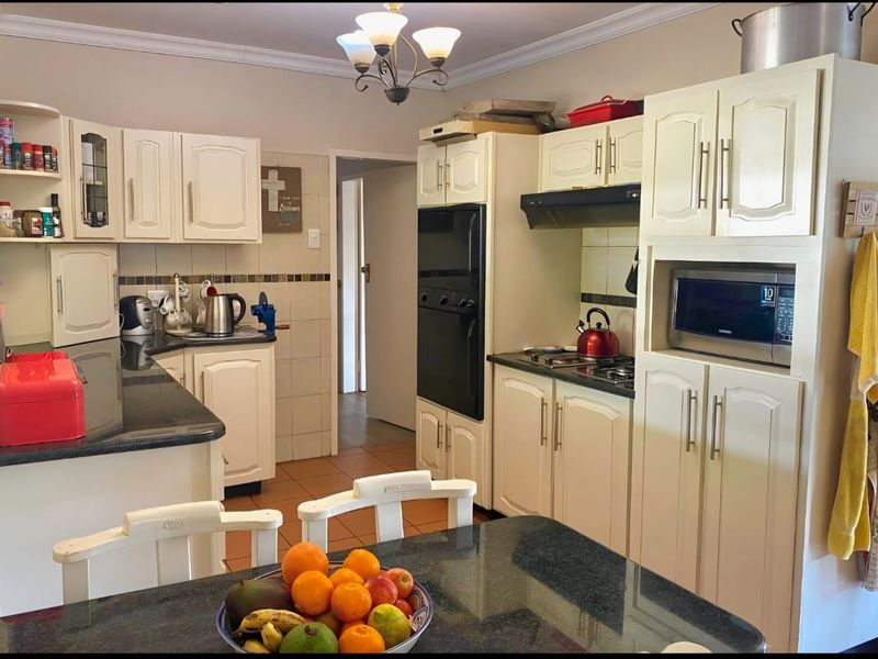 A functional kitchen featuring cream-colored cabinetry, dark granite countertops, built-in oven, hob, and integrated microwave with a tiled backsplash.