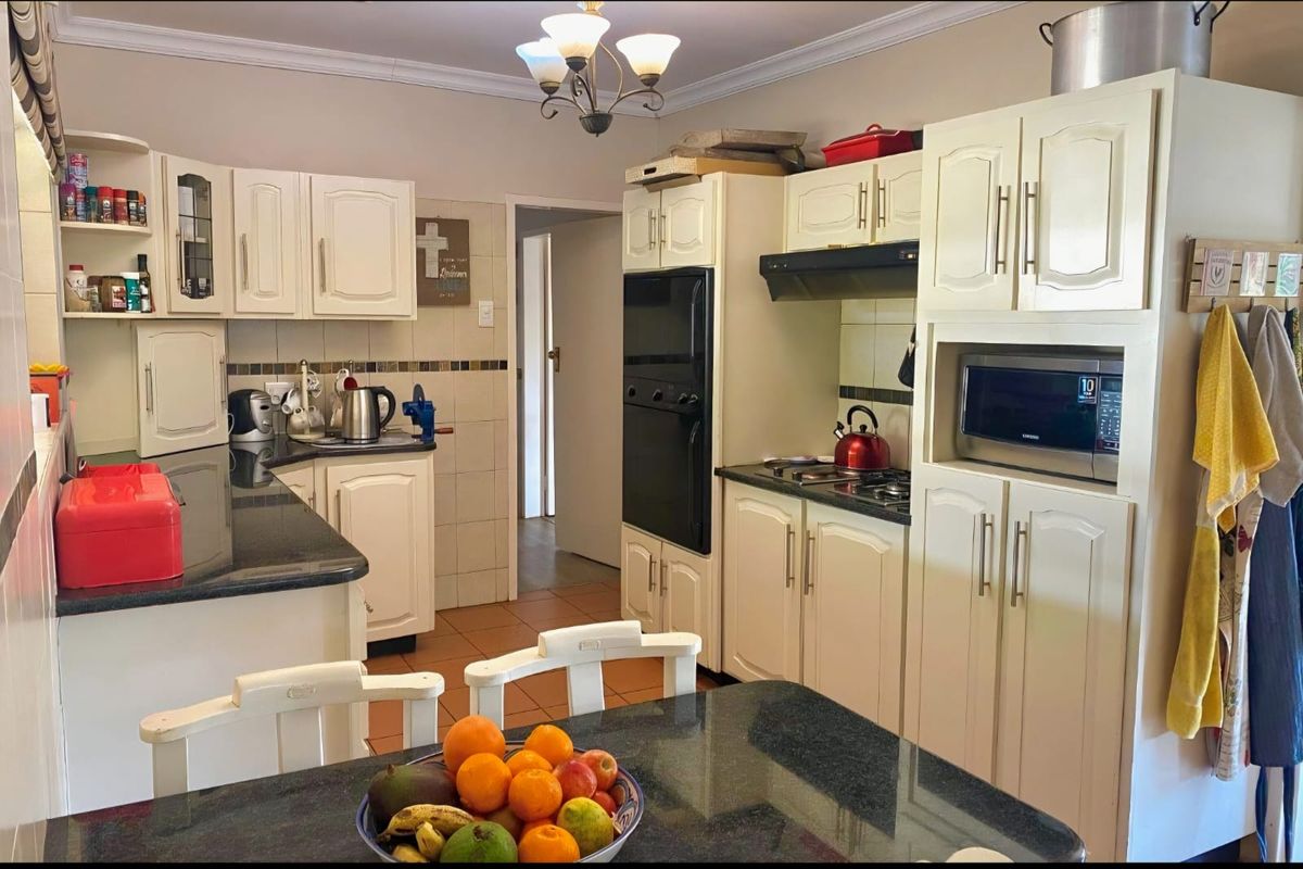 A functional kitchen featuring cream-colored cabinetry, dark granite countertops, built-in oven, hob, and integrated microwave with a tiled backsplash.