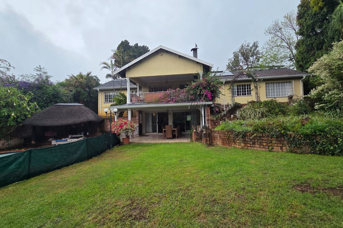 Rear view of a two-story house featuring a balcony, a thatched lapa, and a spacious garden with established landscaping.