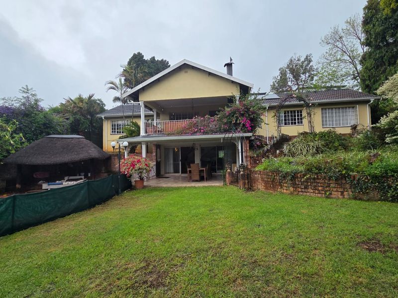 Rear view of a two-story house featuring a balcony, a thatched lapa, and a spacious garden with established landscaping.
