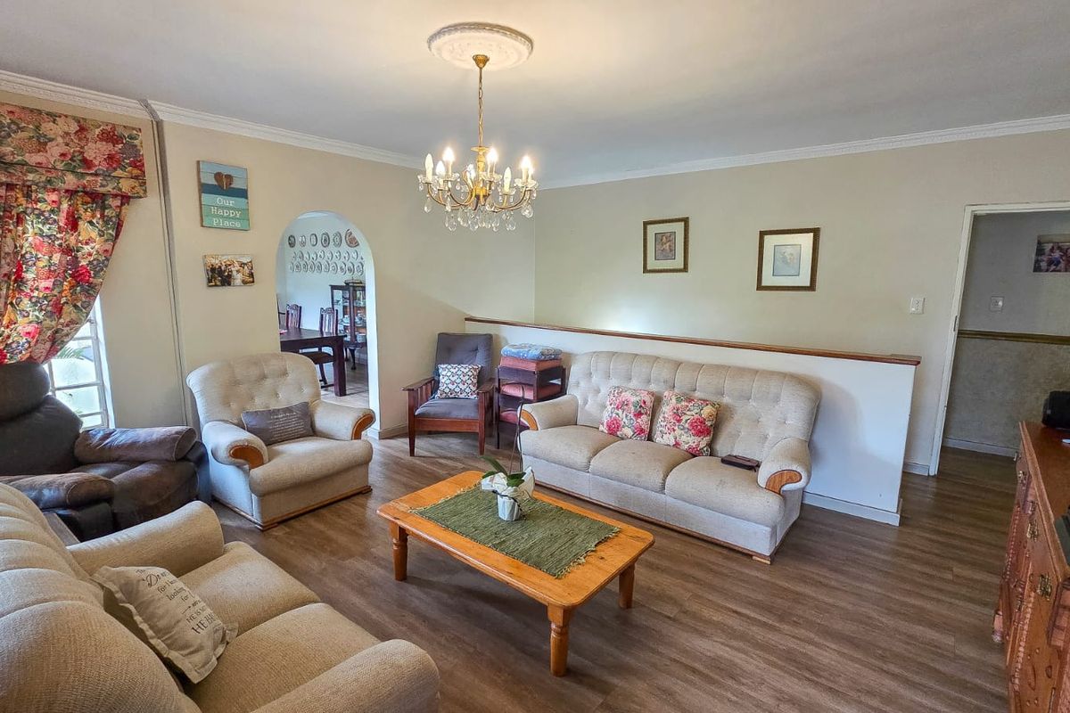 A spacious living room featuring laminate flooring, a decorative ceiling rose with a chandelier, and an arched entryway leading to an adjacent room.
