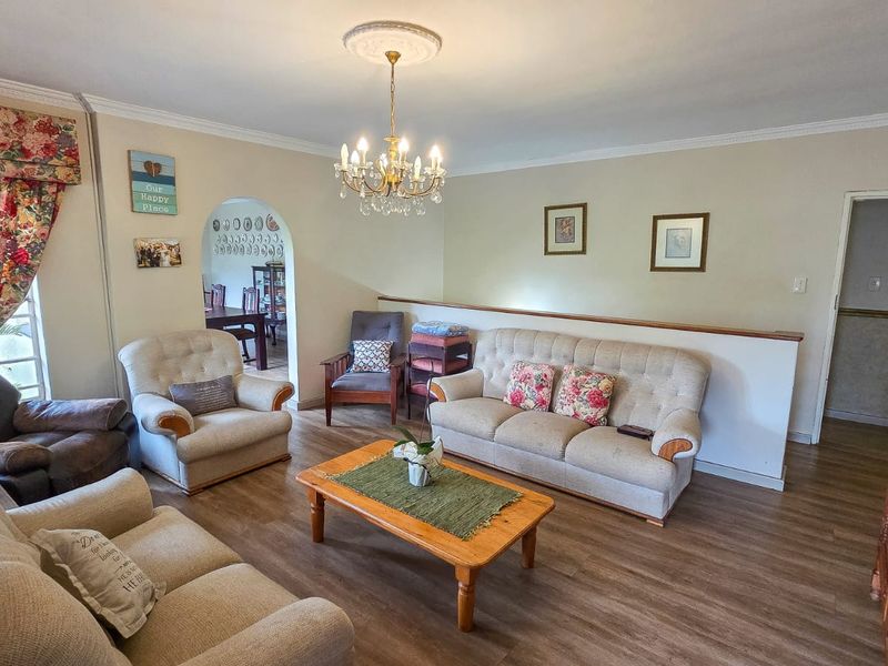 A spacious living room featuring laminate flooring, a decorative ceiling rose with a chandelier, and an arched entryway leading to an adjacent room.