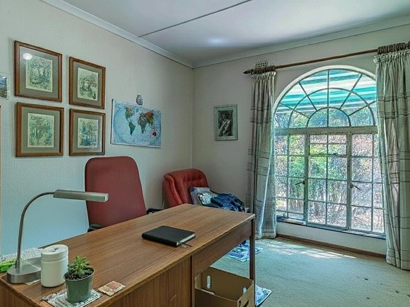 A home office featuring a large arched window that provides natural light and views of the garden.