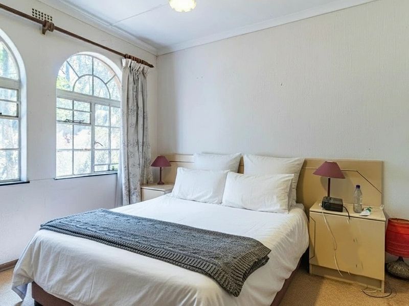 A bedroom featuring distinctive arched windows, a built-in headboard, and carpeted flooring, offering a bright and functional living space.
