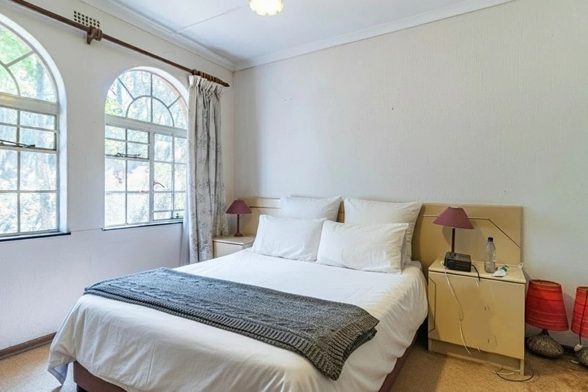 A bedroom featuring distinctive arched windows, a built-in headboard, and carpeted flooring, offering a bright and functional living space.