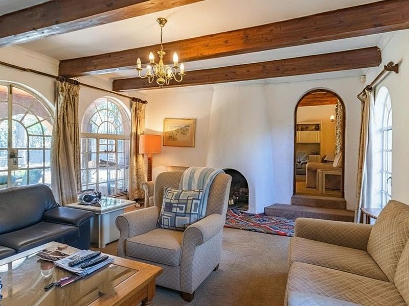 A cozy living room featuring exposed timber ceiling beams, a traditional masonry fireplace, and arched windows that provide natural light.