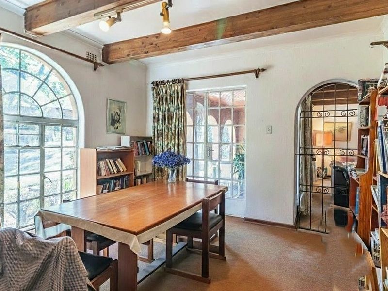 Dining room featuring exposed timber ceiling beams, an arched window, and a wrought iron security gate leading to adjacent living spaces.