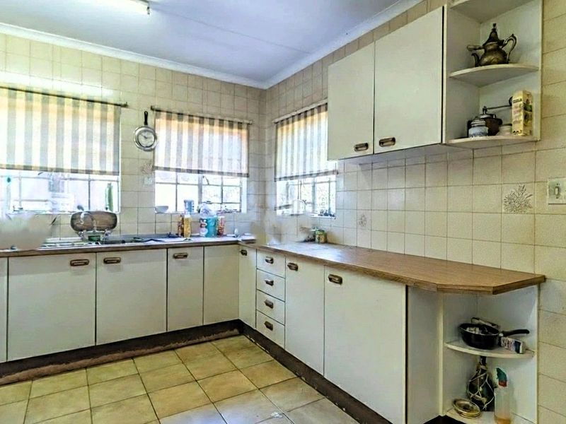 A functional kitchen featuring laminate countertops, tiled splashbacks, and ample built-in cabinetry, offering a dated aesthetic ready for modernization.
