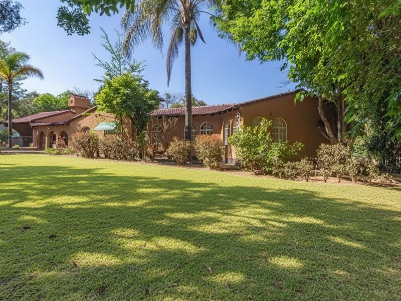 A view of the rear elevation of the house featuring a large, well-maintained lawn and mature garden landscaping.