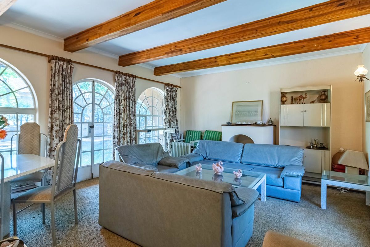 Spacious living room featuring exposed timber ceiling beams, arched windows, and glass doors that provide natural light and access to the exterior.