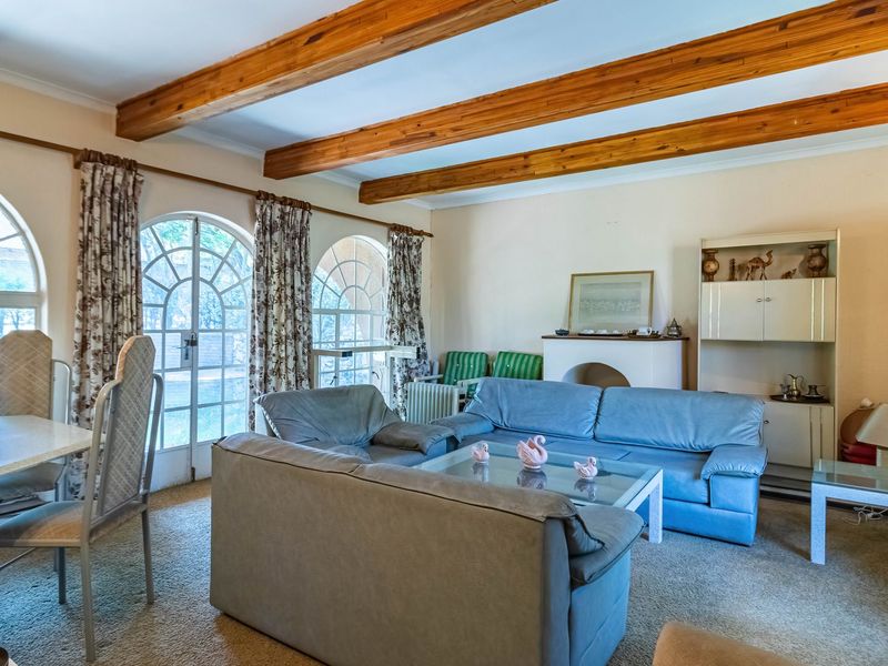 Spacious living room featuring exposed timber ceiling beams, arched windows, and glass doors that provide natural light and access to the exterior.