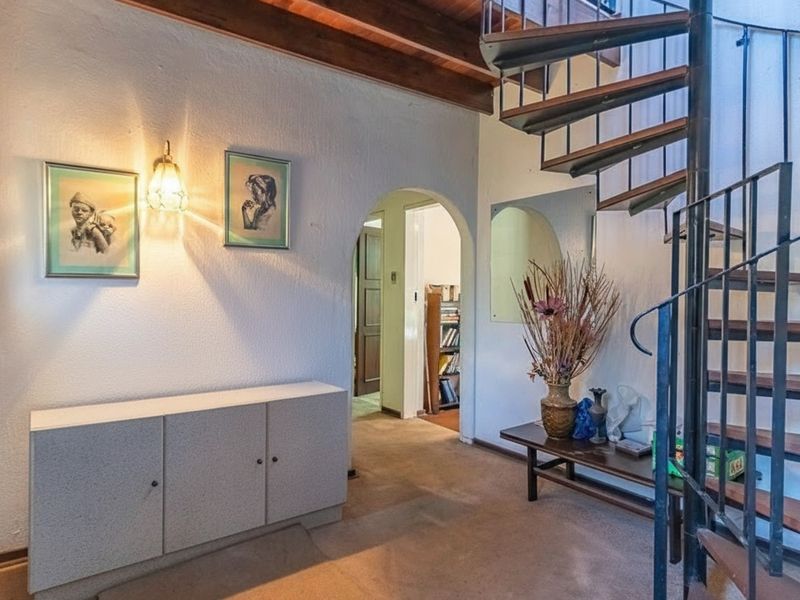 Entrance hall featuring a distinctive spiral staircase, exposed timber ceiling beams, and an arched doorway leading to adjacent living spaces.