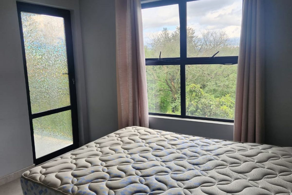 A bright bedroom featuring tiled flooring, recessed lighting, and large aluminium-framed windows and a door providing natural light and outdoor views.