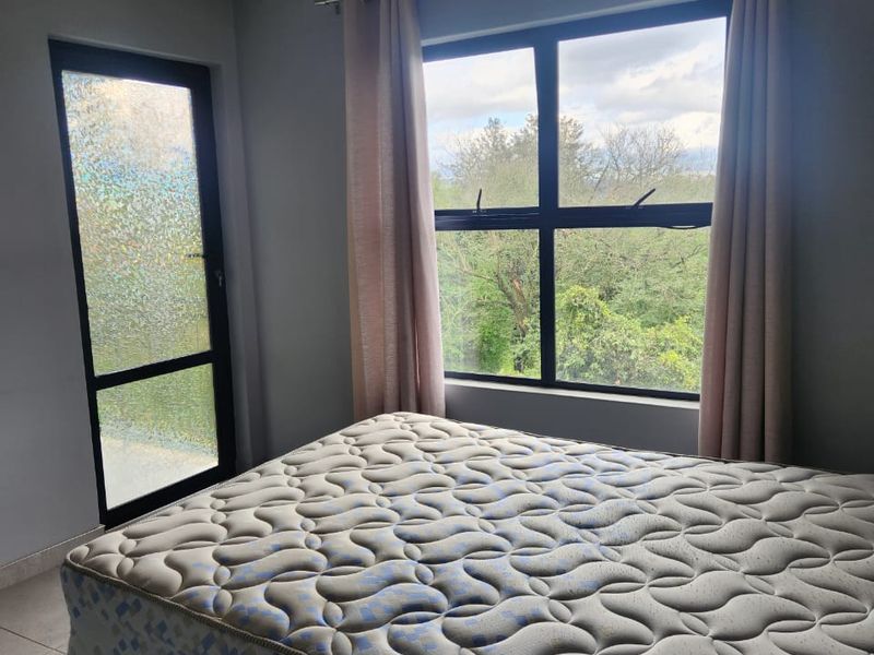A bright bedroom featuring tiled flooring, recessed lighting, and large aluminium-framed windows and a door providing natural light and outdoor views.