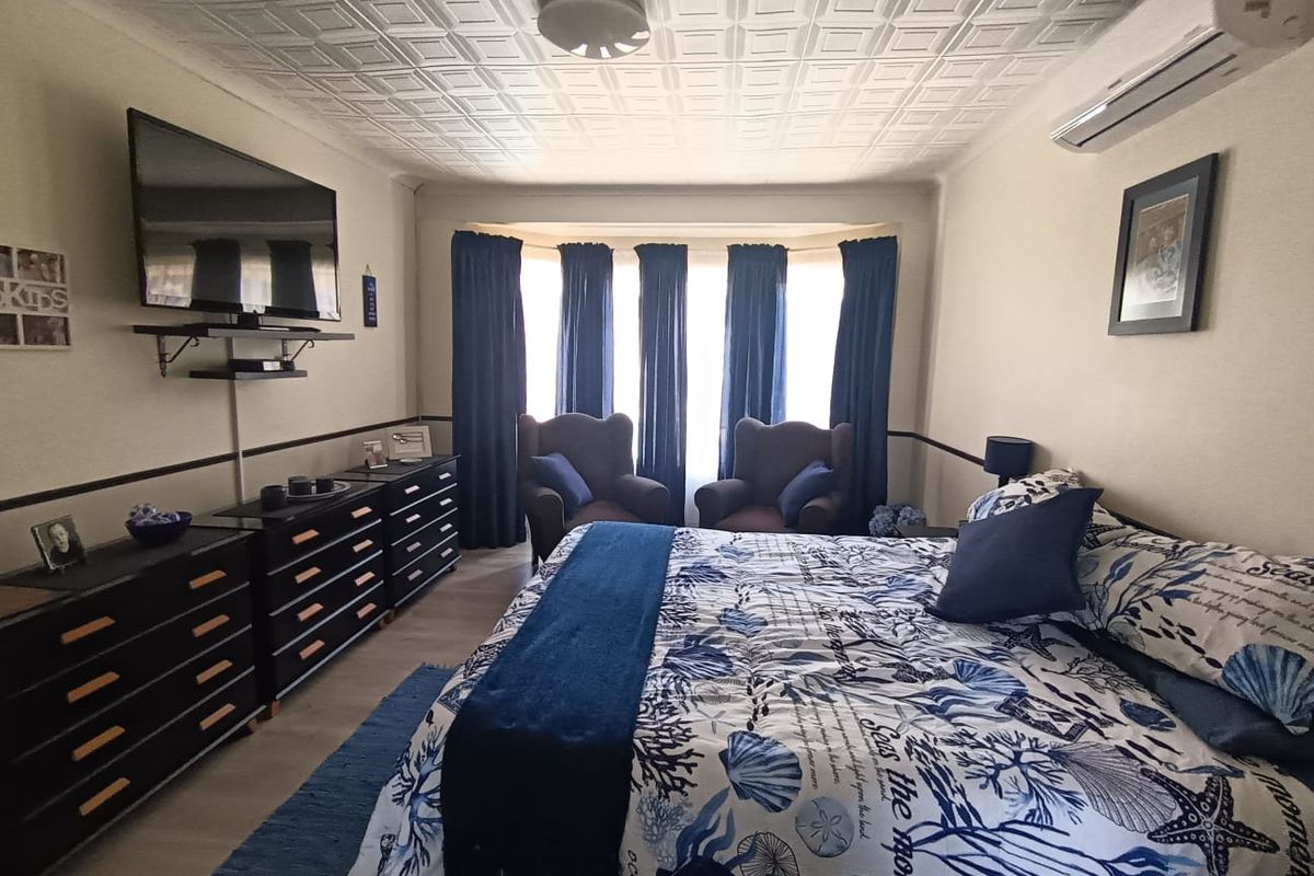 A well-maintained bedroom featuring a coffered ceiling, wall-mounted air conditioning unit, and a large bay window with integrated curtain tracks.