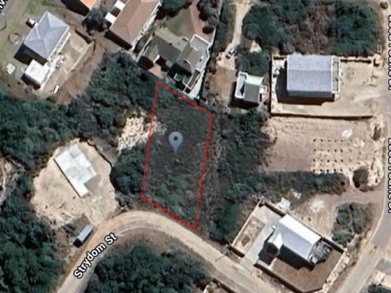 Aerial view of a vacant residential plot highlighted in red, situated within a developed neighborhood with surrounding street access.