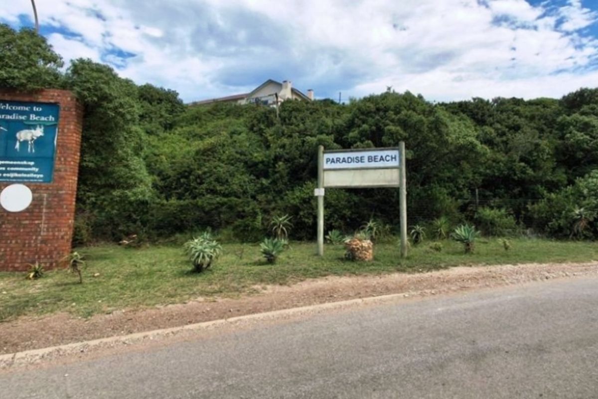 Street view of the Paradise Beach entrance featuring a brick signage wall and local community information boards.