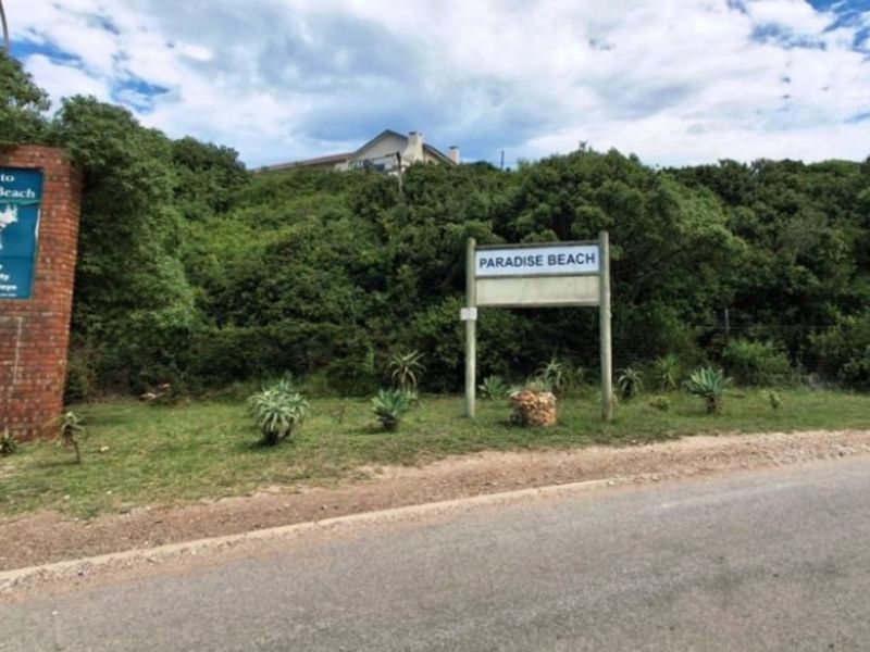 Street view of the Paradise Beach entrance featuring a brick signage wall and local community information boards.