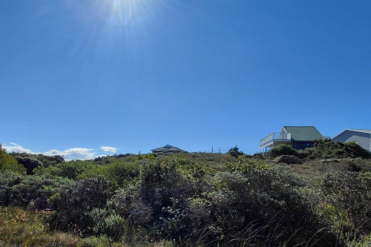 A view of the vacant residential land featuring natural coastal vegetation and a sloped landscape with neighboring properties visible in the distance.