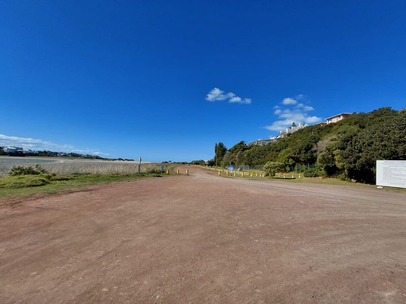 A view of an unpaved access road leading towards the coast, surrounded by natural vegetation and nearby residential properties.