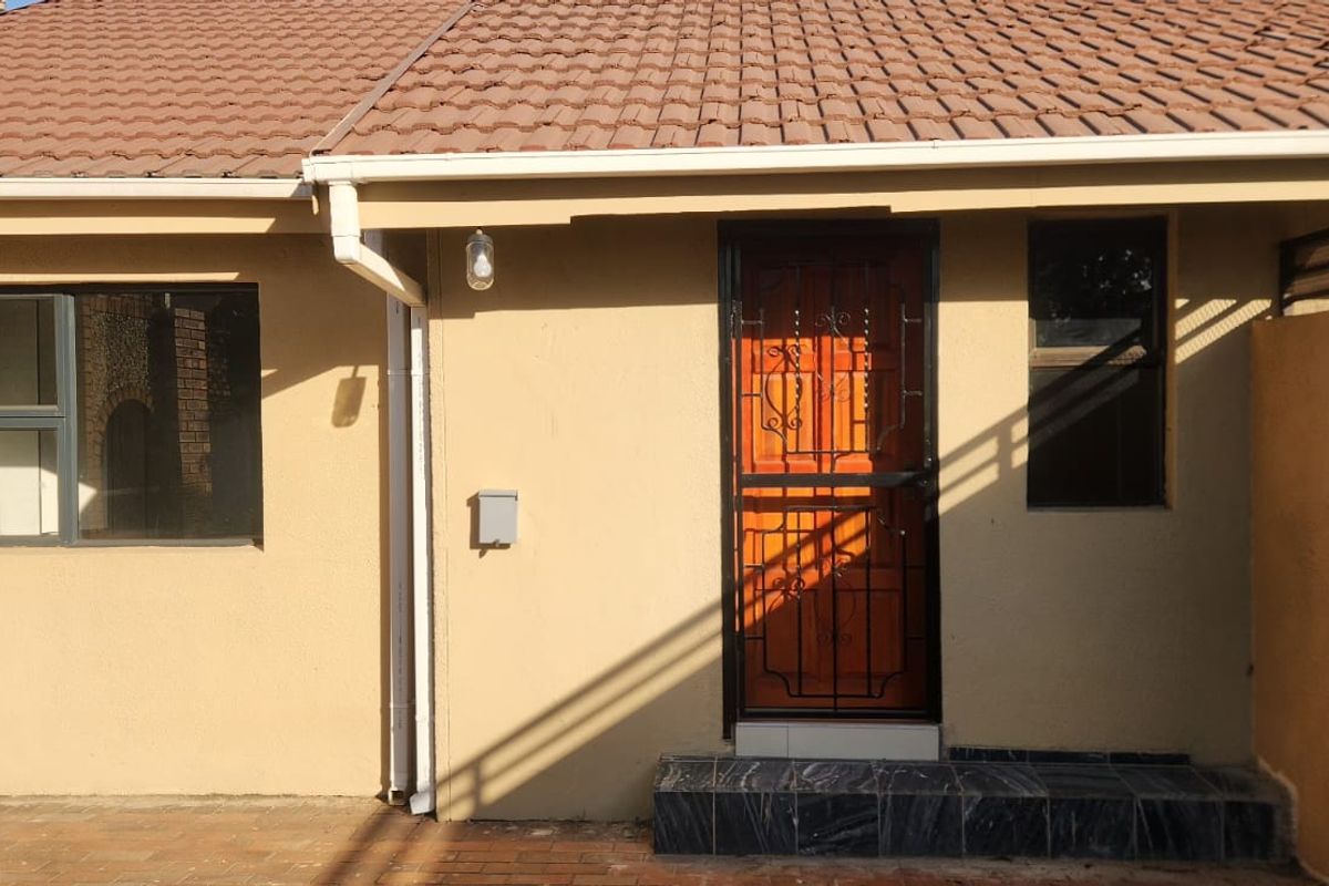 Rear exterior view of the property featuring a paved patio area, security gate, and tiled roof.
