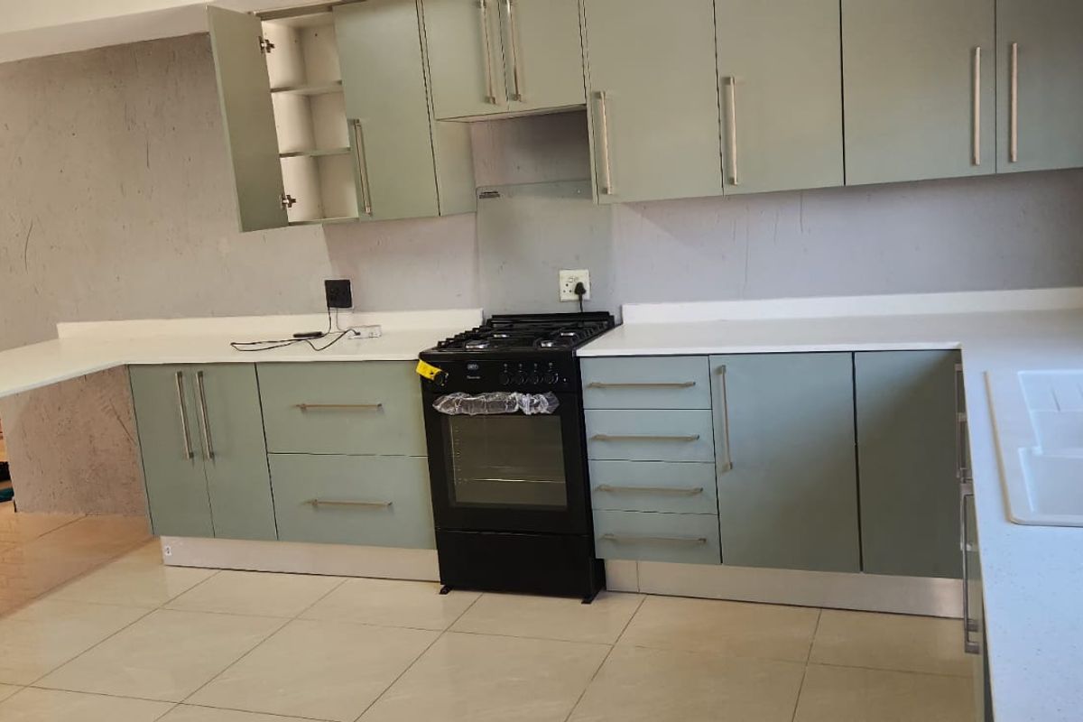 A modern kitchen featuring sage green cabinetry, white quartz countertops, a black freestanding oven, and a double basin sink, requiring final wall finishing.