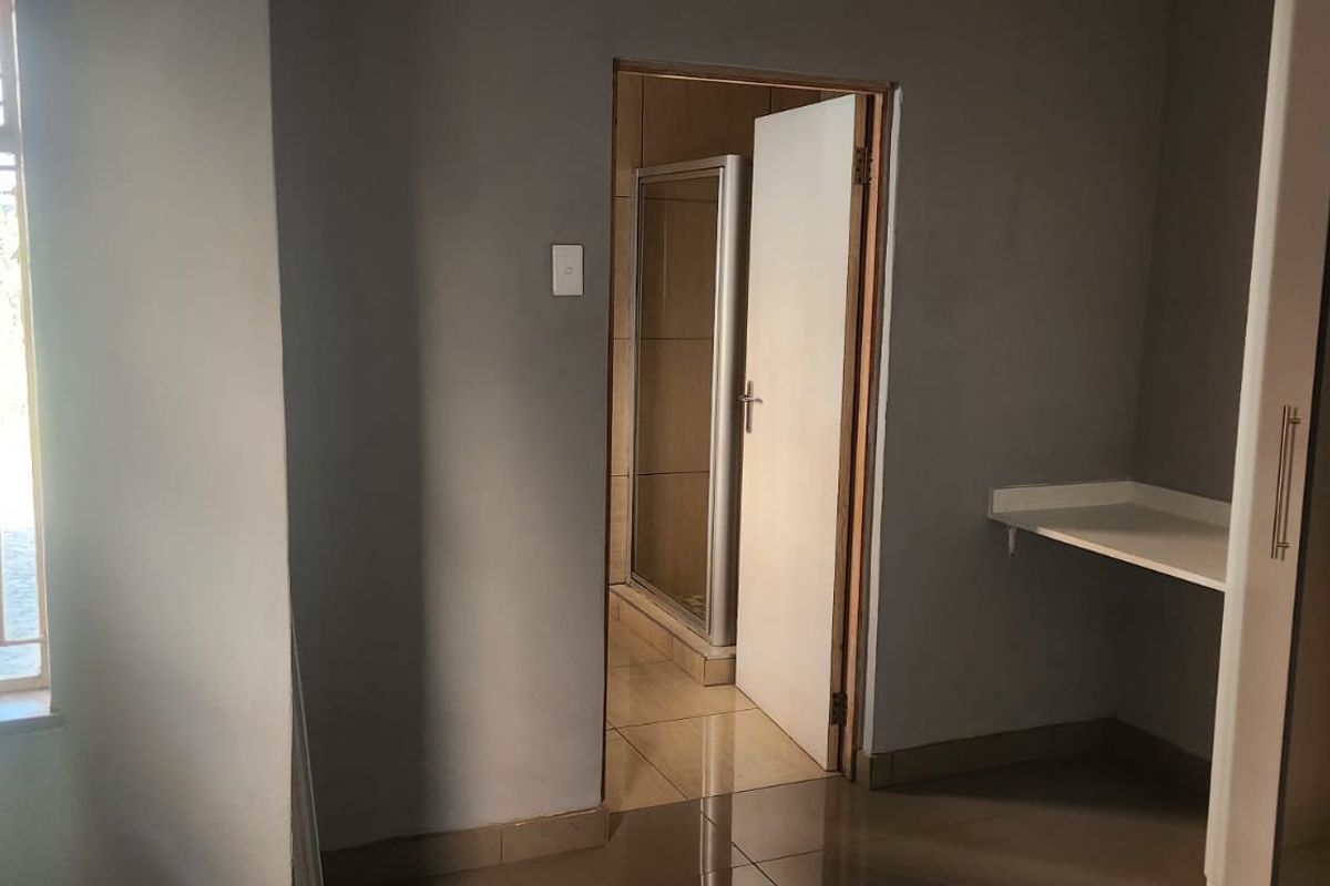 A functional bedroom featuring built-in cupboards, a built-in desk, tiled flooring, and direct access to an en-suite bathroom.