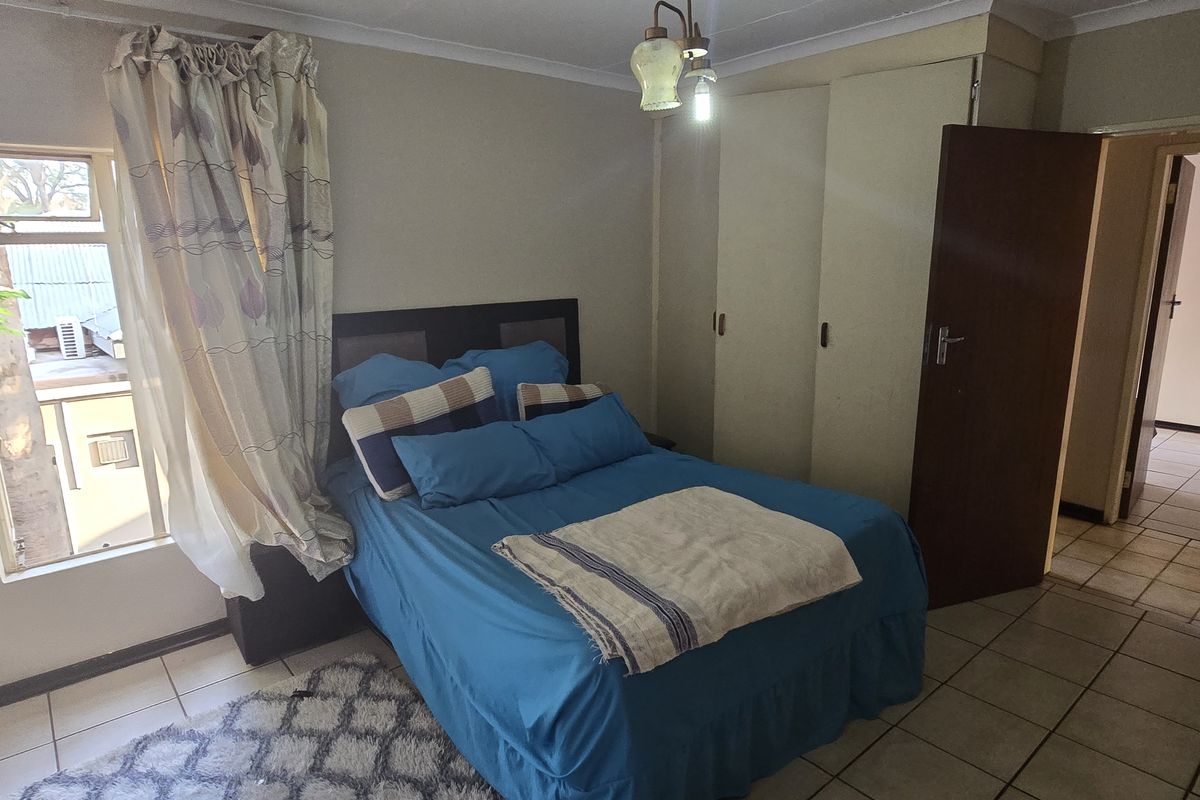 A bedroom featuring built-in cupboards, tiled flooring, and natural light from a side window, providing a functional living space.