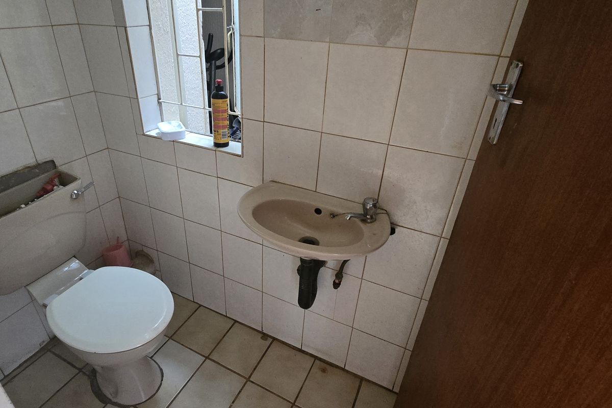 A compact guest bathroom featuring a wall-mounted basin and toilet, finished with dated ceramic wall and floor tiling.