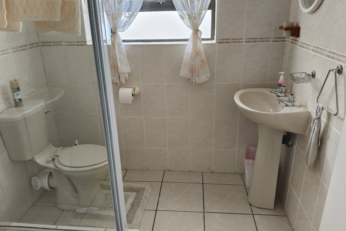 A functional bathroom featuring a pedestal basin, a glass-enclosed shower, and neutral wall and floor tiling.