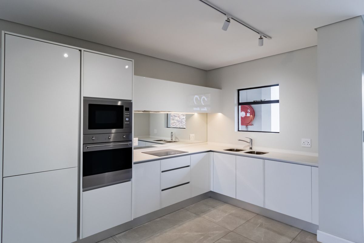 Modern kitchen featuring sleek white cabinetry, integrated oven and microwave, induction hob, mirrored splashback, and tiled flooring.