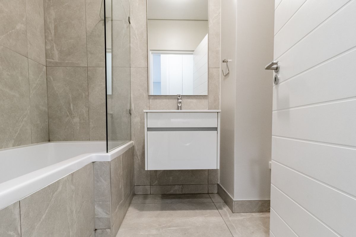 Modern bathroom featuring a wall-mounted vanity, a bathtub with a glass shower screen, and neutral large-format floor and wall tiles.