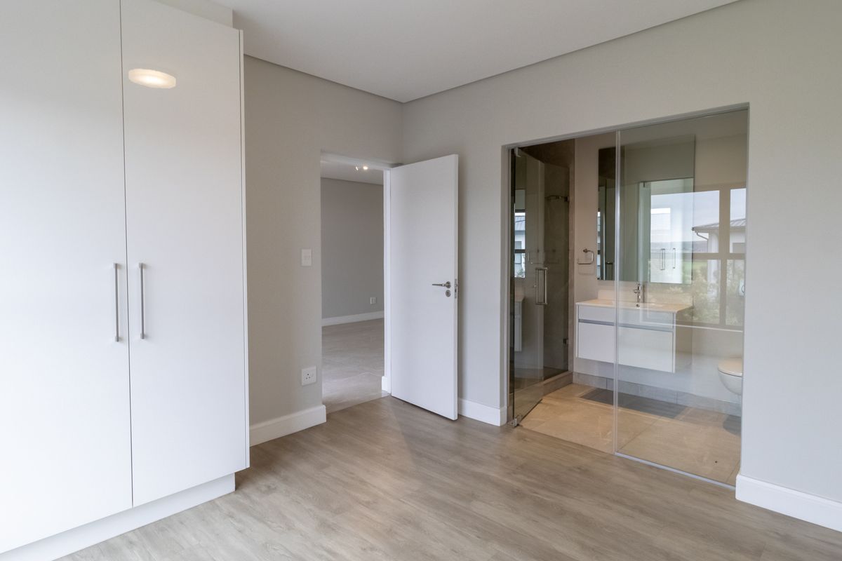 Modern bedroom featuring built-in cupboards, wood-look flooring, and an en-suite bathroom with a glass partition wall.