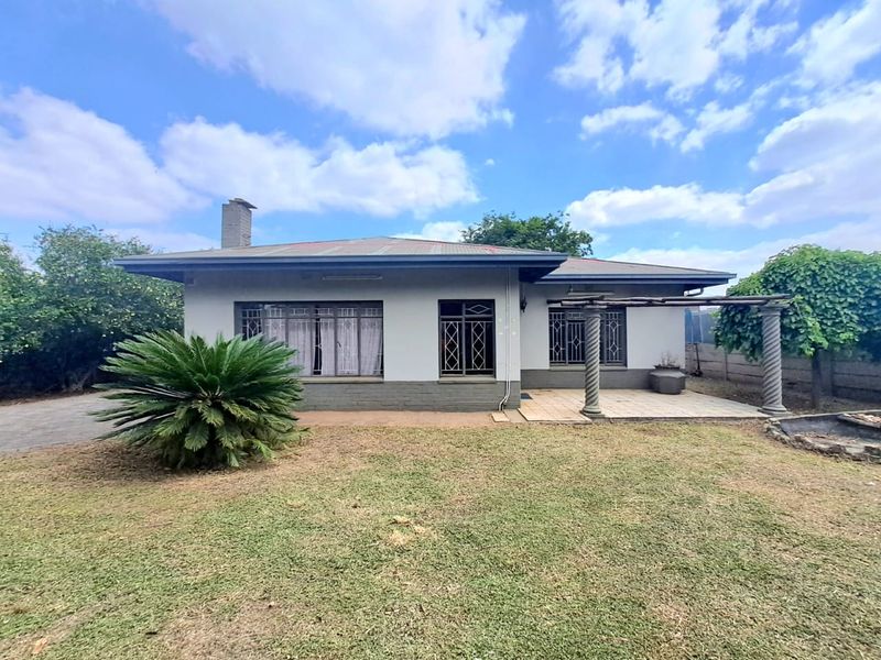 Rear view of a single-story house featuring a tiled patio, decorative columns, and security bars on the windows, set within a garden area.
